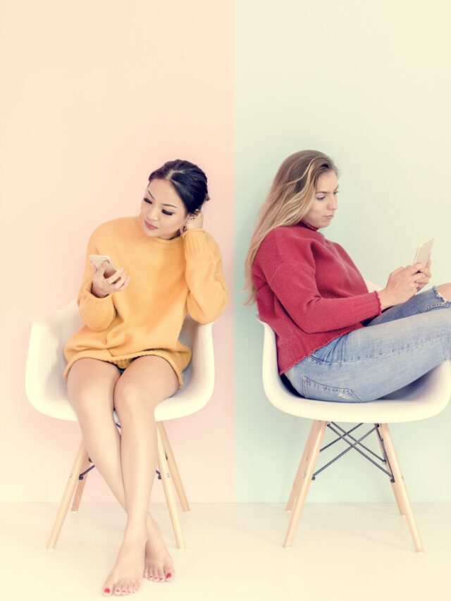 Caucasian and asian women sitting using mobile phones together with pink and mint green background